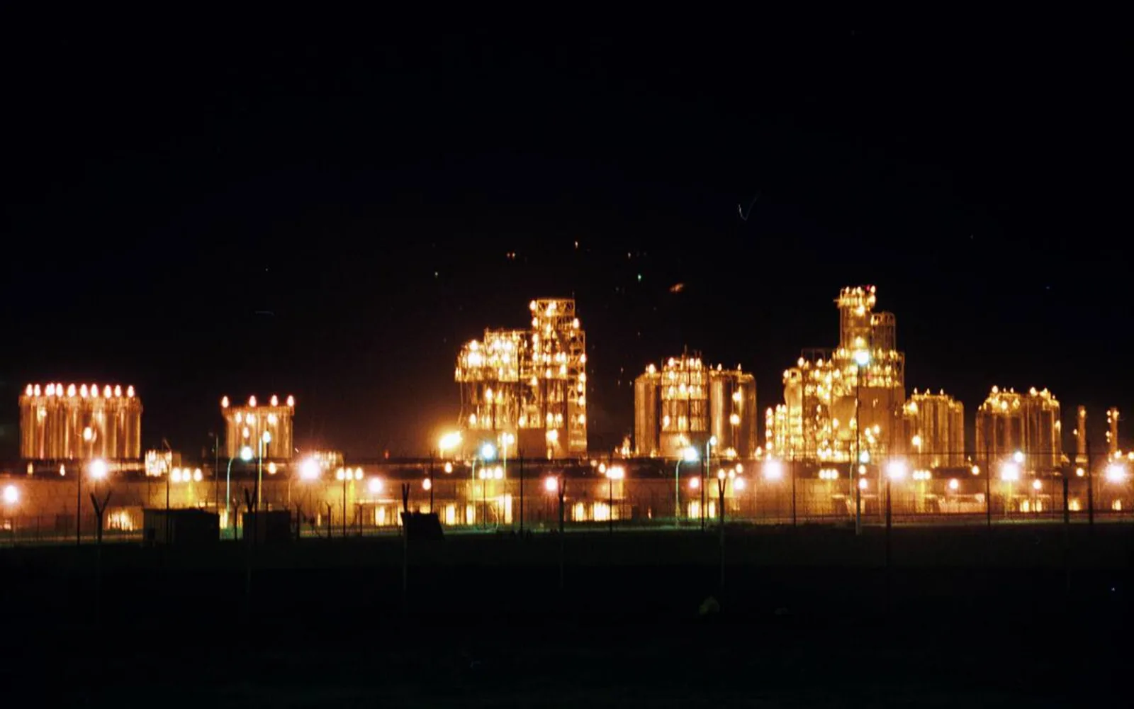Industrial oil refinery complex at night with illuminated towers and processing equipment silhouetted against the dark sky